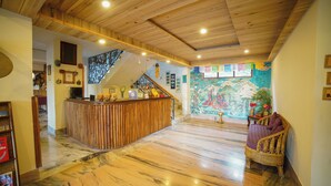 A reception area with a wooden reception desk, a staircase, and a mural on the wall. - Bamboo Retreat Hotel (Gangtok)