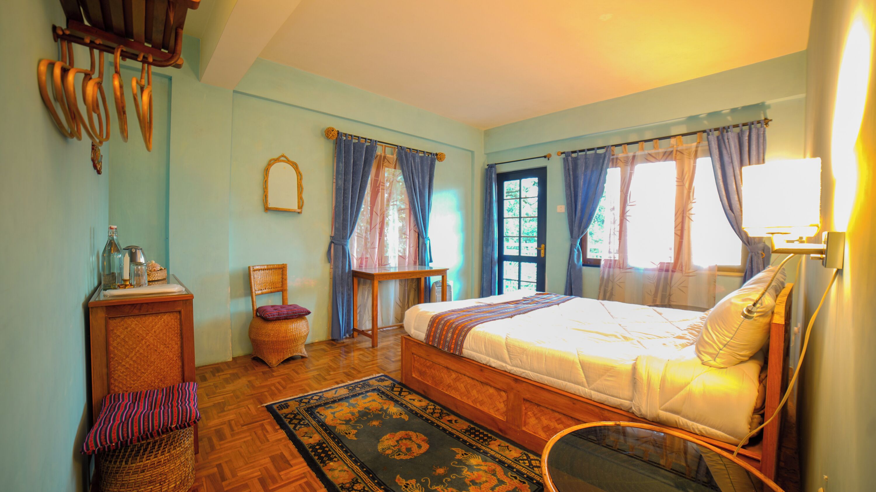 Une chambre à coucher avec un lit, une chaise, une petite table, un miroir et une fenêtre avec des rideaux.
