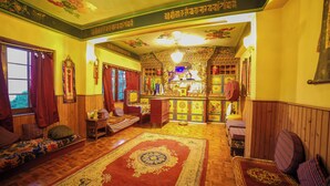 A traditional room with a wooden floor, a red patterned rug, a sofa, a chair, and a small altar with religious items. - Bamboo Retreat Hotel (Gangtok)