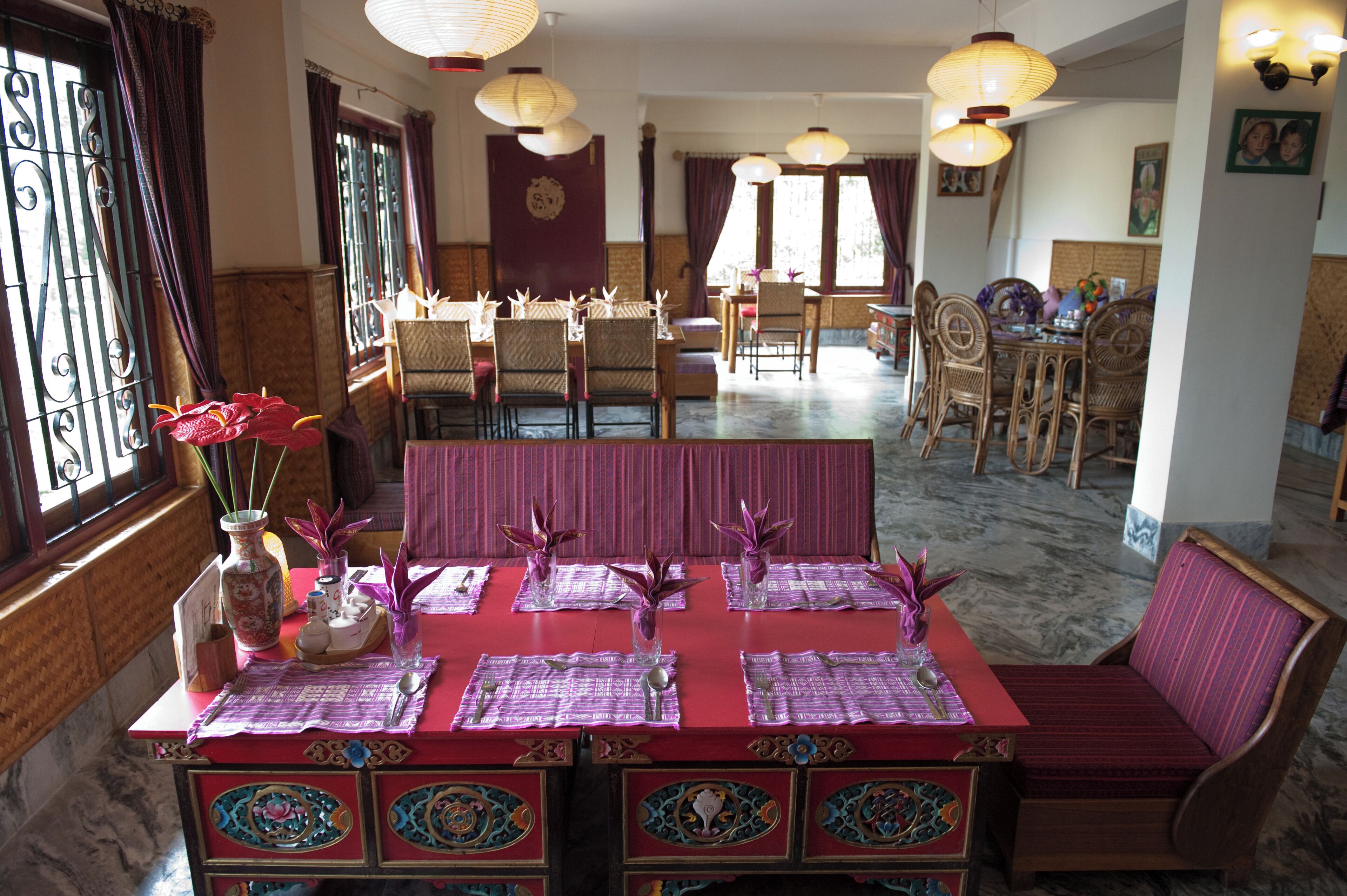 Een eetgedeelte met een rode tafel, paarse placemats en rieten stoelen.