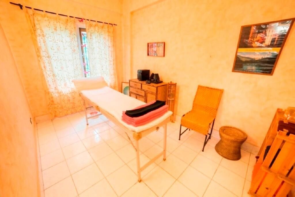 Un consultorio médico con una cama, un armario de madera, una silla y un cesto de basura.