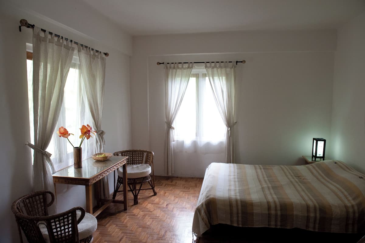 A room with a bed, a table with chairs, a vase with flowers, and a lamp.