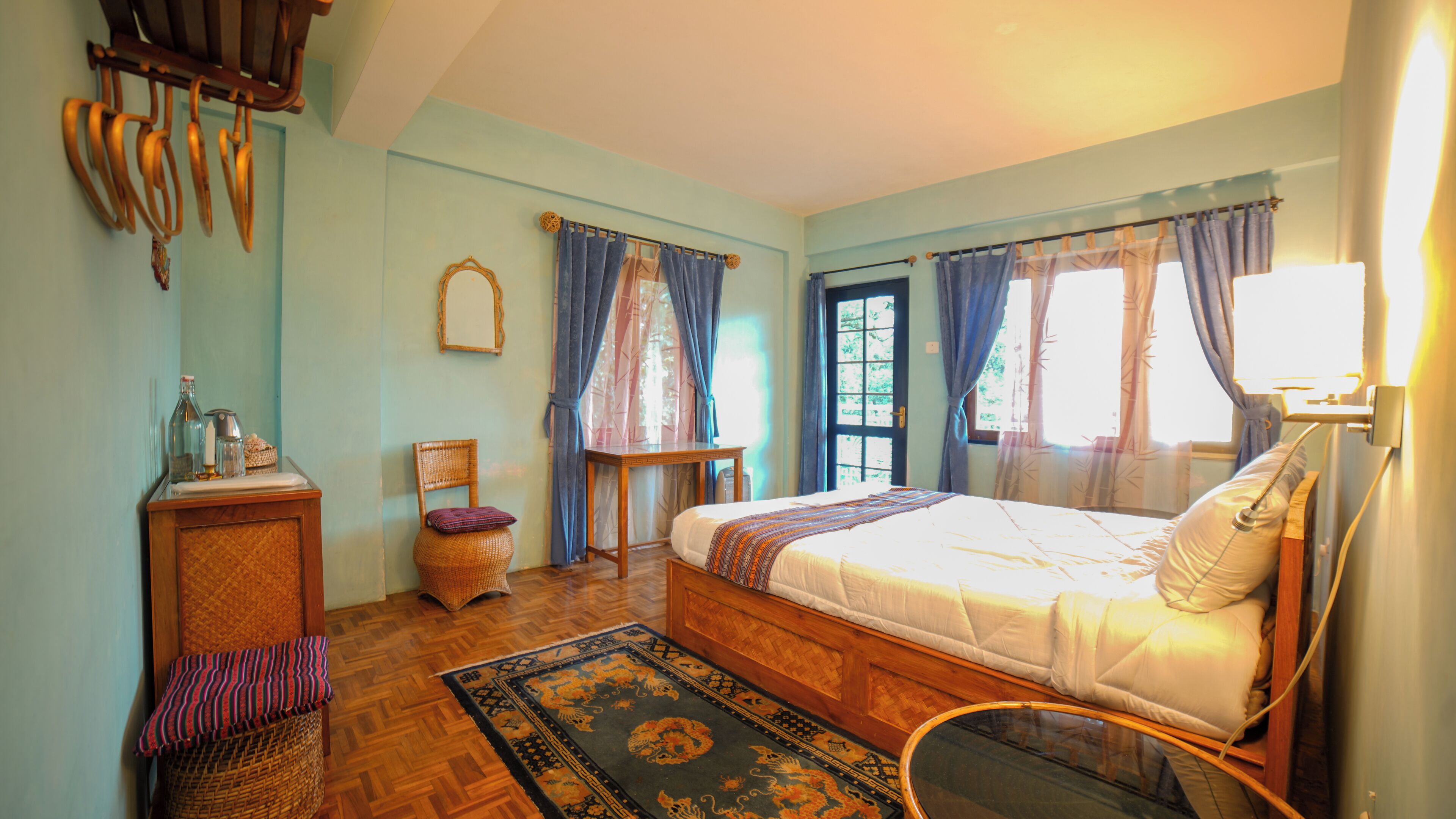 A bedroom with a bed, a chair, a small table, a mirror, and a window with curtains.