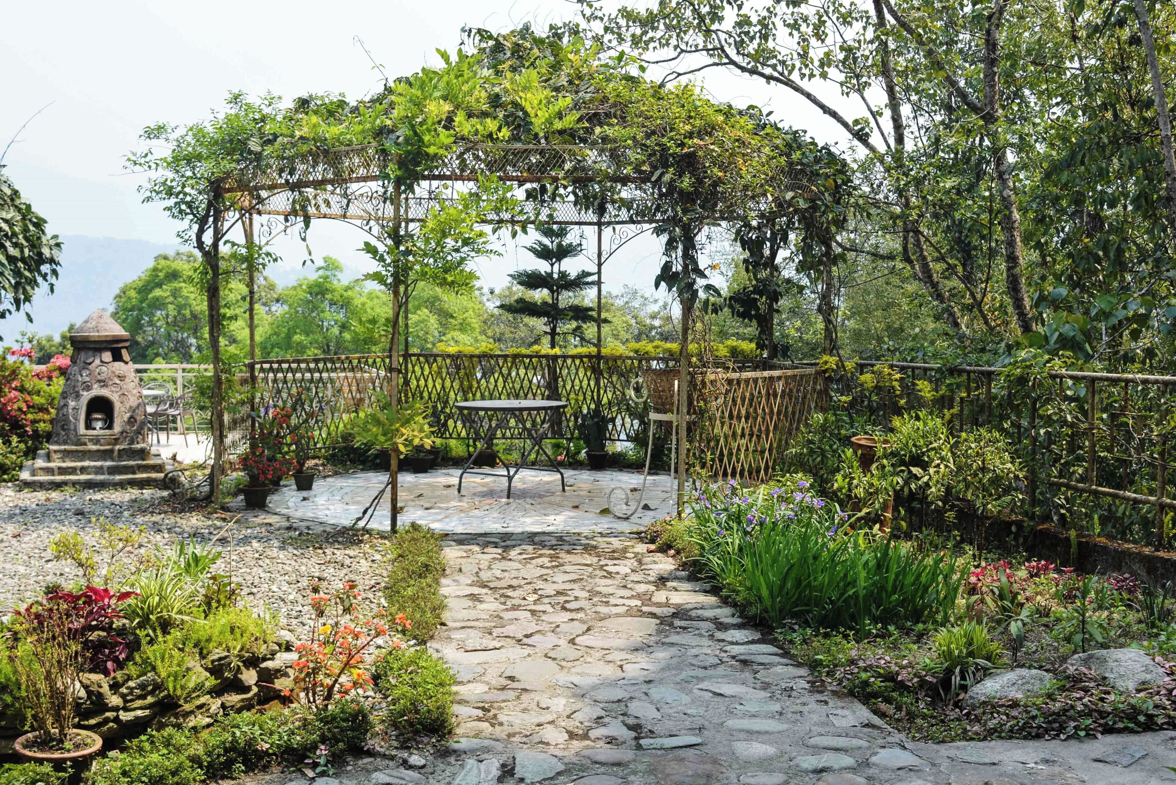 A garden with a stone pathway, a pergola, and a small stone structure.