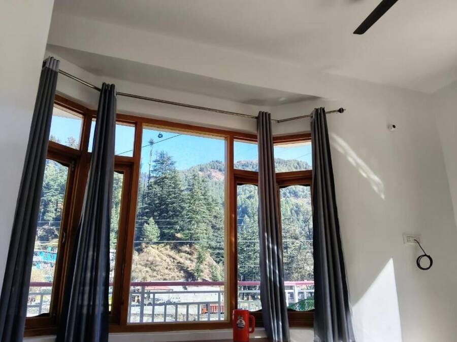 Quarto com grandes janelas, cortinas e vista para uma área arborizada.
