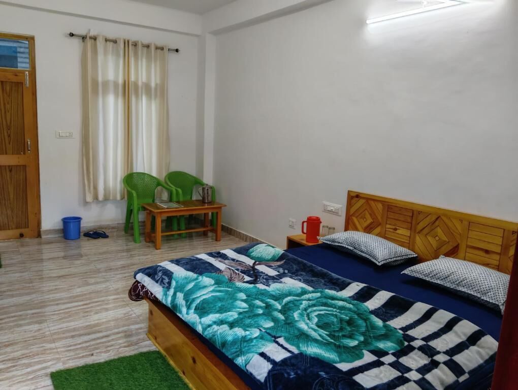 A bedroom with a bed, a wooden headboard, a green chair, a small table, and a window with curtains.