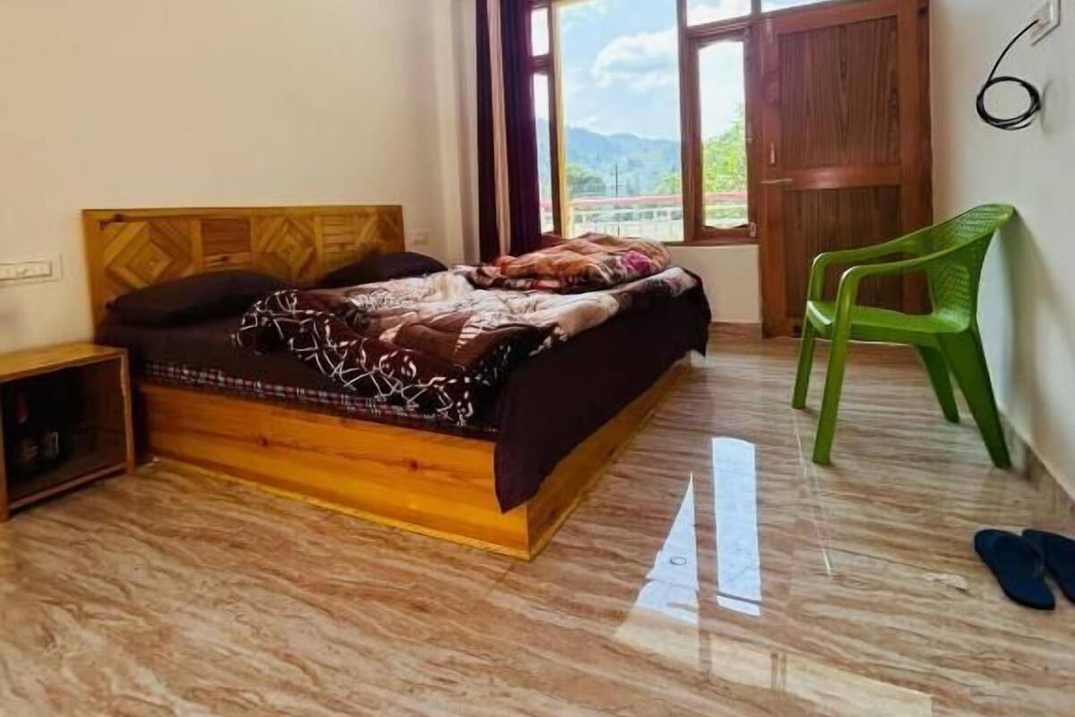 A bedroom with a bed, a ceiling fan, a window with curtains, a green chair, and a pair of slippers on the floor.