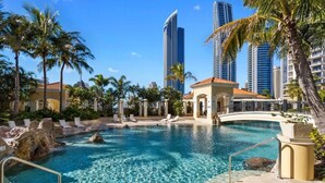 Zona de piscina con agua cristalina, palmeras y edificios altos al fondo.