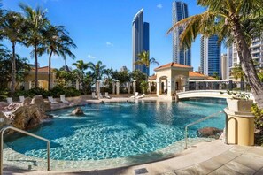 A pool area with clear water, palm trees, and high-rise buildings in the background. - Luxury 3BR Ocean View Apartment | Walk to Beach (Surfers Paradise)