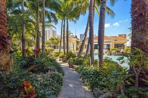 A pathway leading to a pool area surrounded by palm trees and lush greenery. - Luxury 3BR Ocean View Apartment | Walk to Beach (Surfers Paradise)