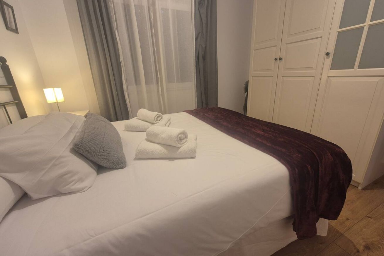 Een hotelkamer met een bed, nachtkastje, lamp, raam met gordijnen en een kledingkast.