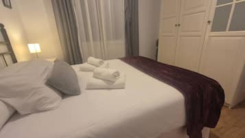Een hotelkamer met een bed, nachtkastje, lamp, raam met gordijnen en een kledingkast.