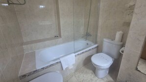 Et badeværelse med badekar, toilet og bruser.