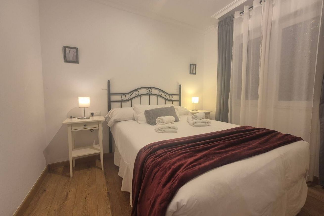 Een slaapkamer met een bed, twee nachtkastjes, een wandlamp en een raam met gordijnen.
