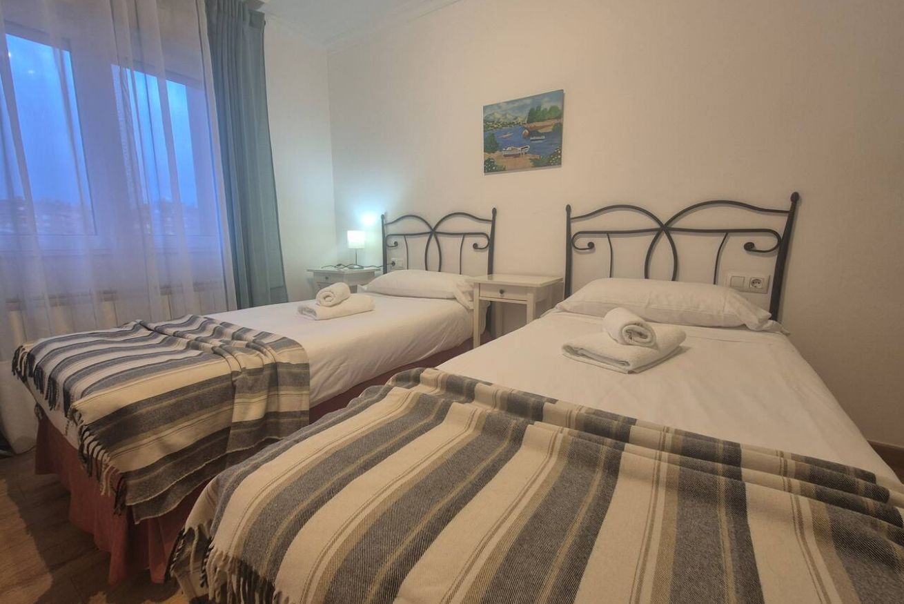 A room with two beds, a painting on the wall, and a window with curtains.