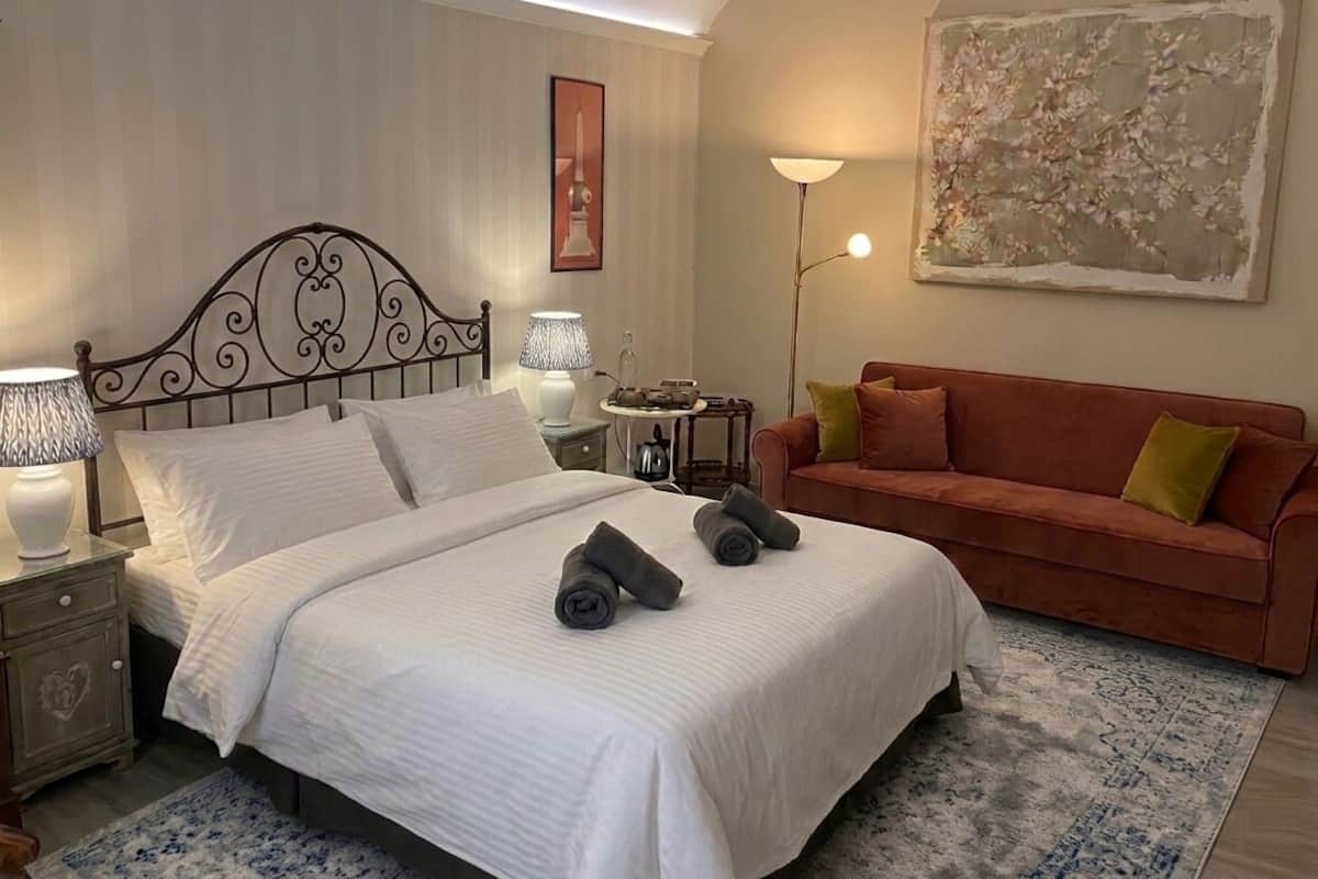 A hotel room with a bed, a nightstand, a lamp, a couch, and a painting on the wall.