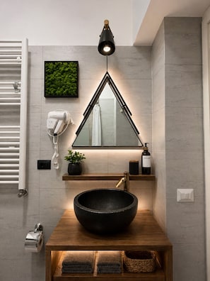 A modern bathroom with a large mirror, a round black sink, a hairdryer, a towel rack, a potted plant, and a wall-mounted light fixture. - Conte Residence (Rome)
