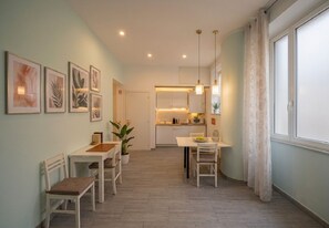 A dining area with a kitchen in the background, a potted plant, and a window with curtains. - Conte Residence (Rome)