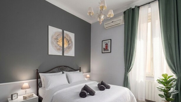 A bedroom with a bed, nightstand, lamp, artwork, and curtains. - Conte Residence (Rome)