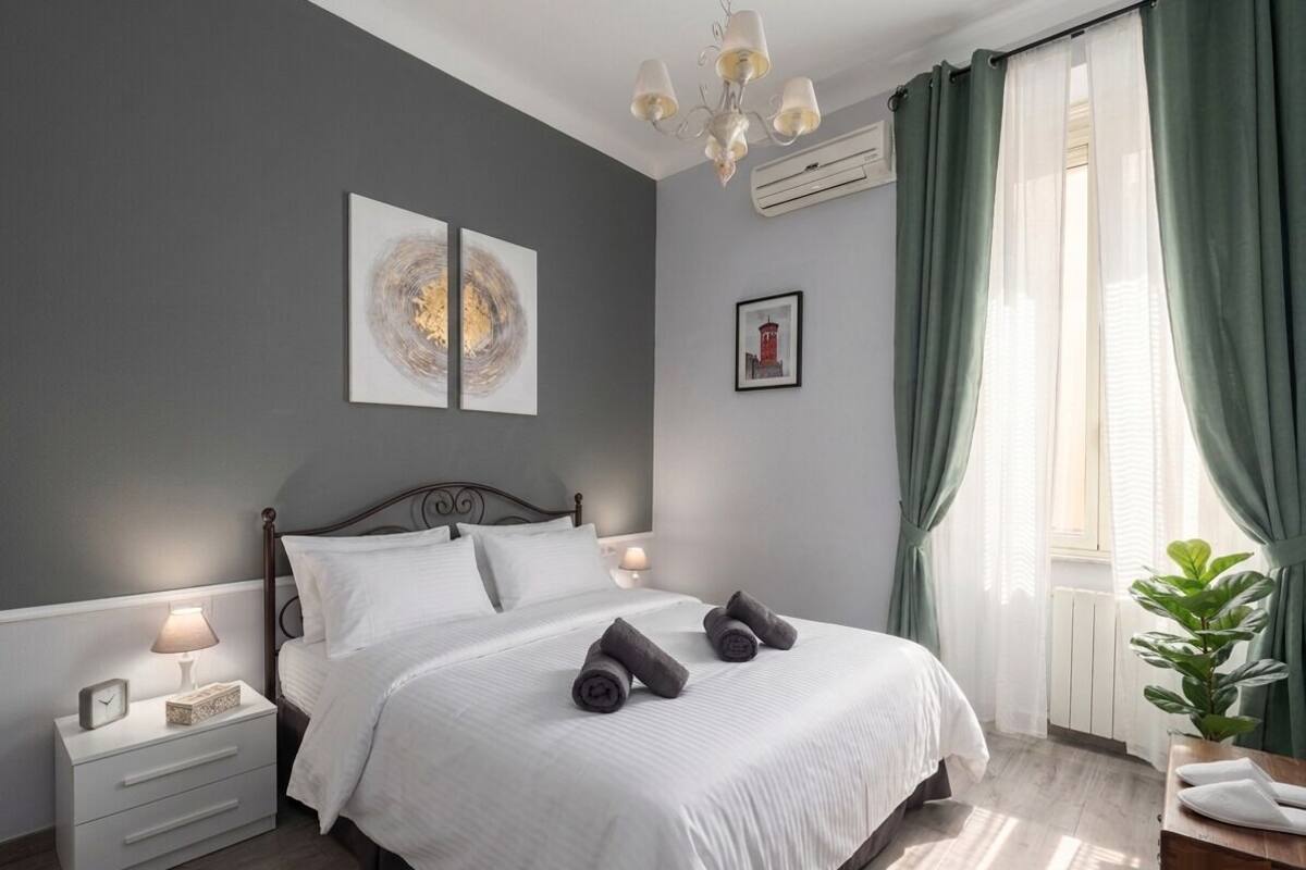 A bedroom with a bed, nightstand, lamp, artwork, and curtains.