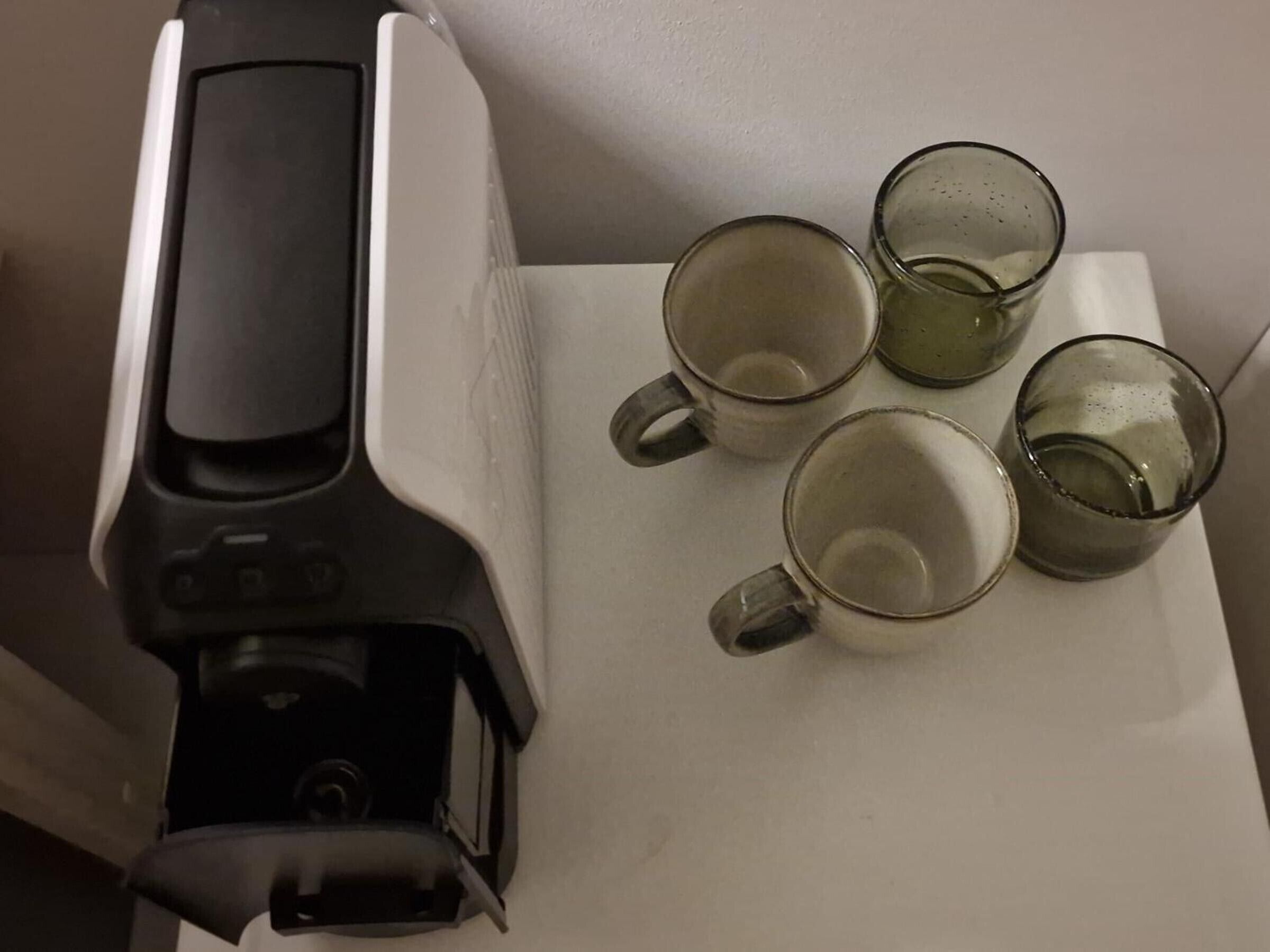 A coffee maker with four empty glass mugs on a white surface.