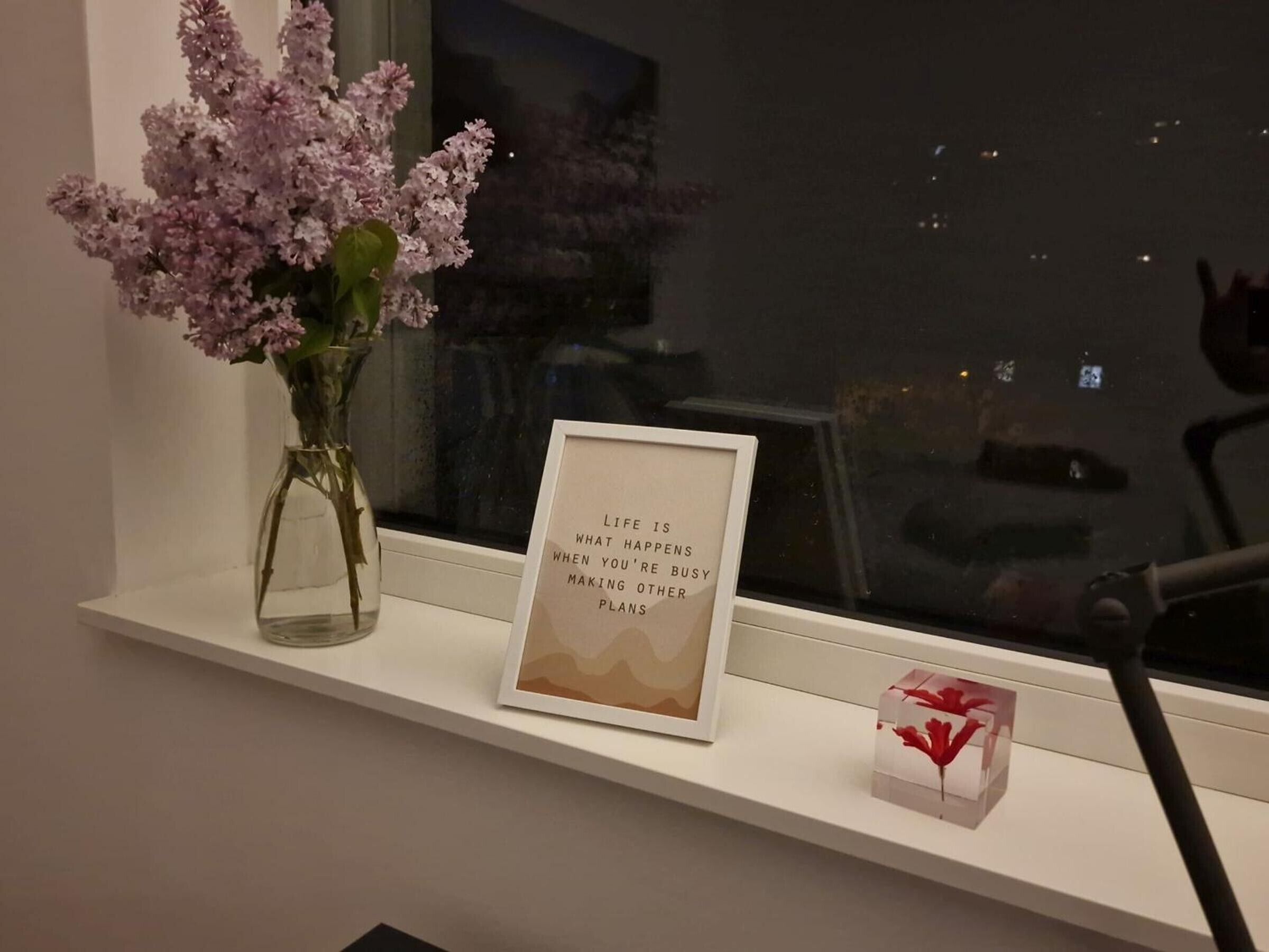 Ein Fensterbrett mit einer Blumenvase, einem gerahmten Motivationsspruch und einem kleinen Dekoartikel.
