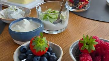 Ein Frühstückstisch mit verschiedenen Speisen, darunter Schalen mit Joghurt, Beeren und einem Käsescheibchen.