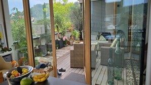 Un patio moderno al aire libre con mobiliario de mimbre, una mesa de comedor con fruta y una zona cerrada con vidrio que tiene una barbacoa.