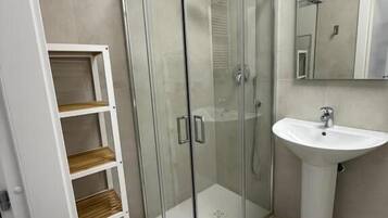 Une salle de bain moderne avec une douche à parois de verre, un lavabo sur colonne blanc et une étagère en bois.