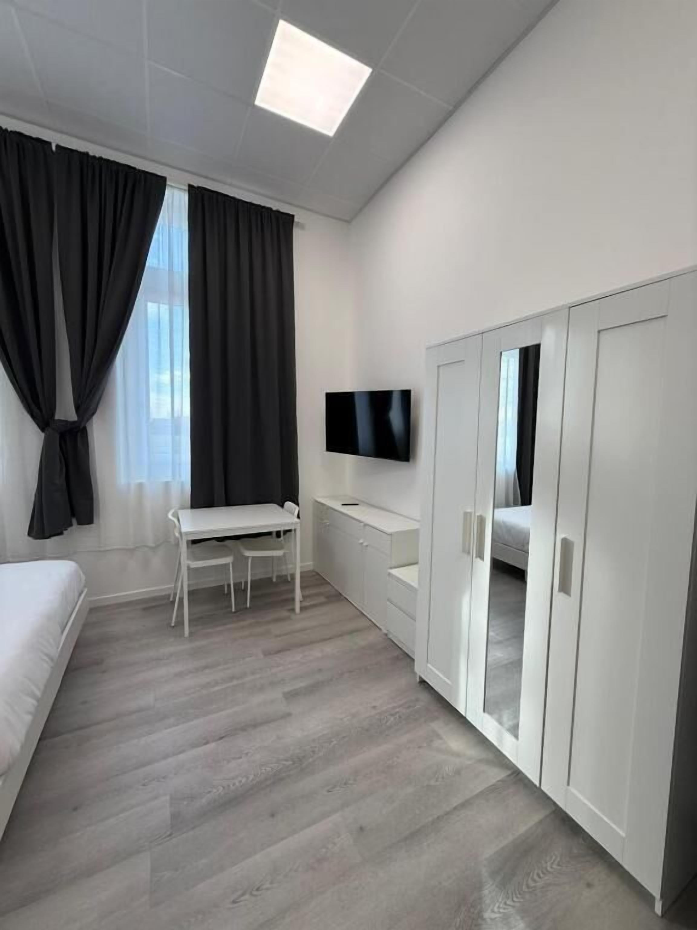 Quarto moderno e minimalista com cama, escrivaninha, televisão e guarda-roupa.