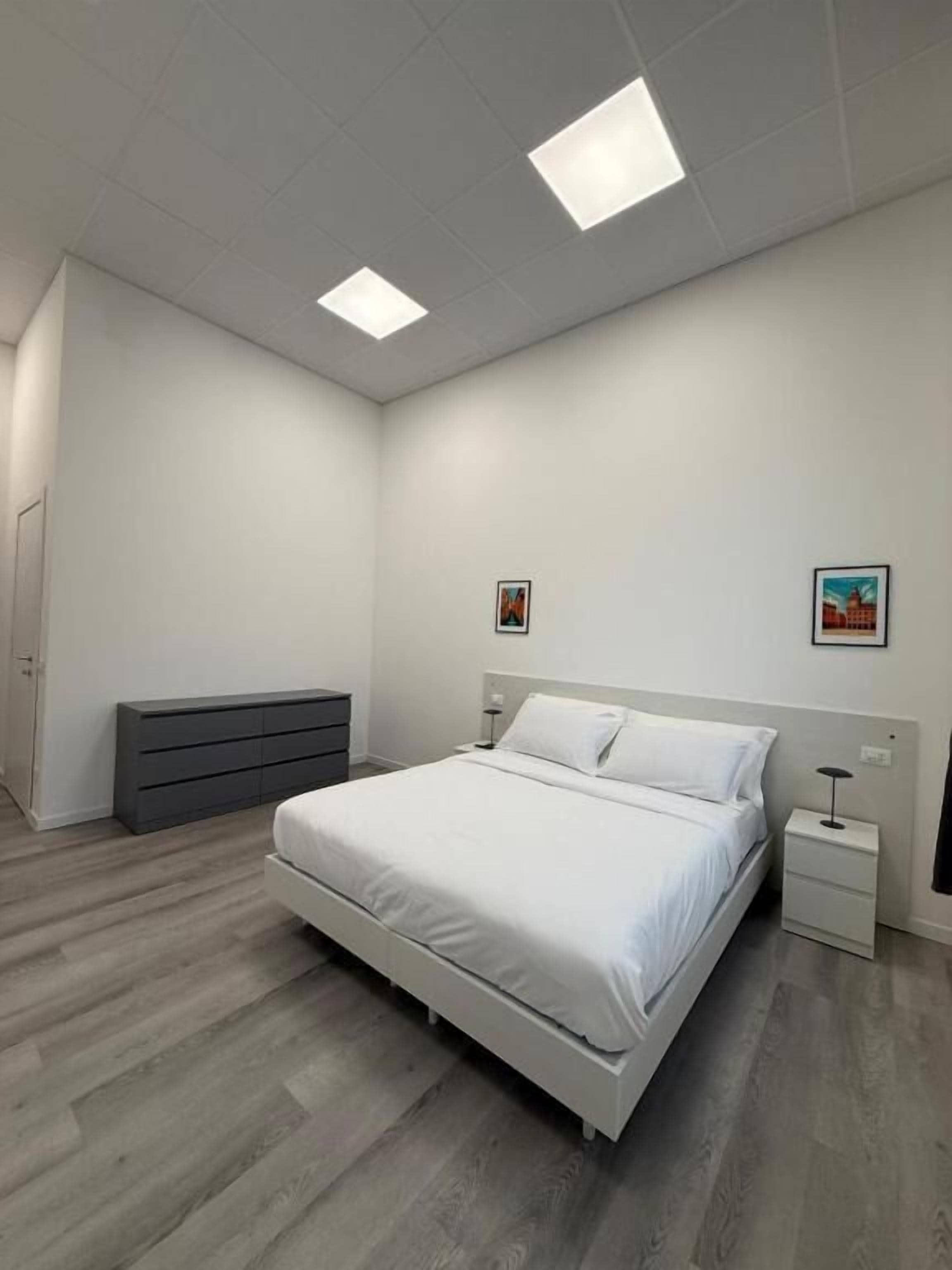 A modern bedroom with a bed, bedside tables, a dresser, and two wall-mounted lights.