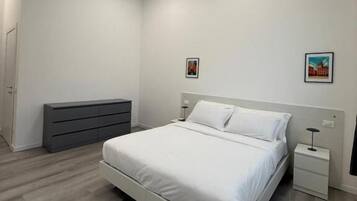 A modern bedroom with a bed, bedside tables, a dresser, and two wall-mounted lights.