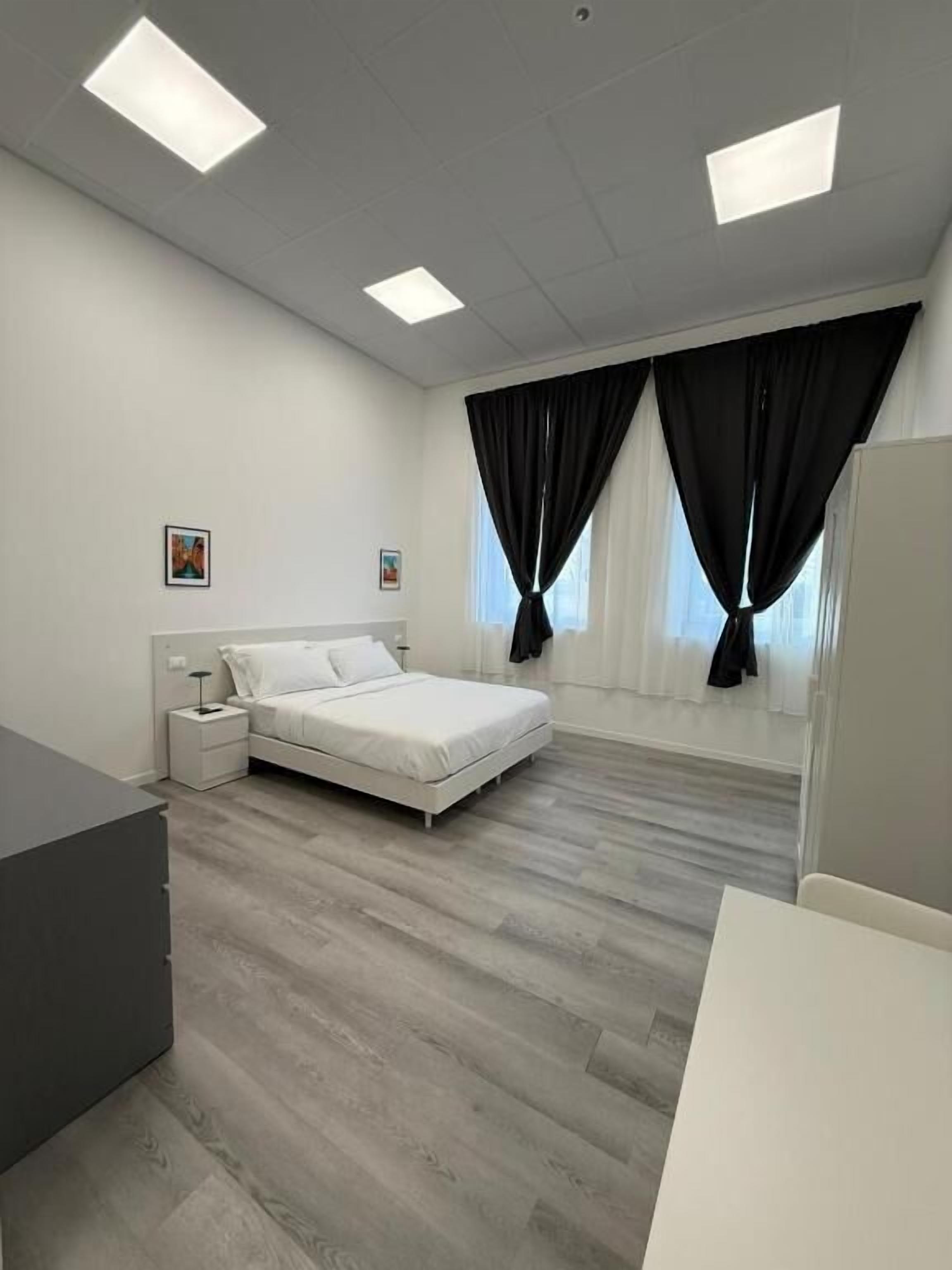 Une chambre à coucher avec un lit, des tables de chevet, un bureau et une fenêtre avec des rideaux.
