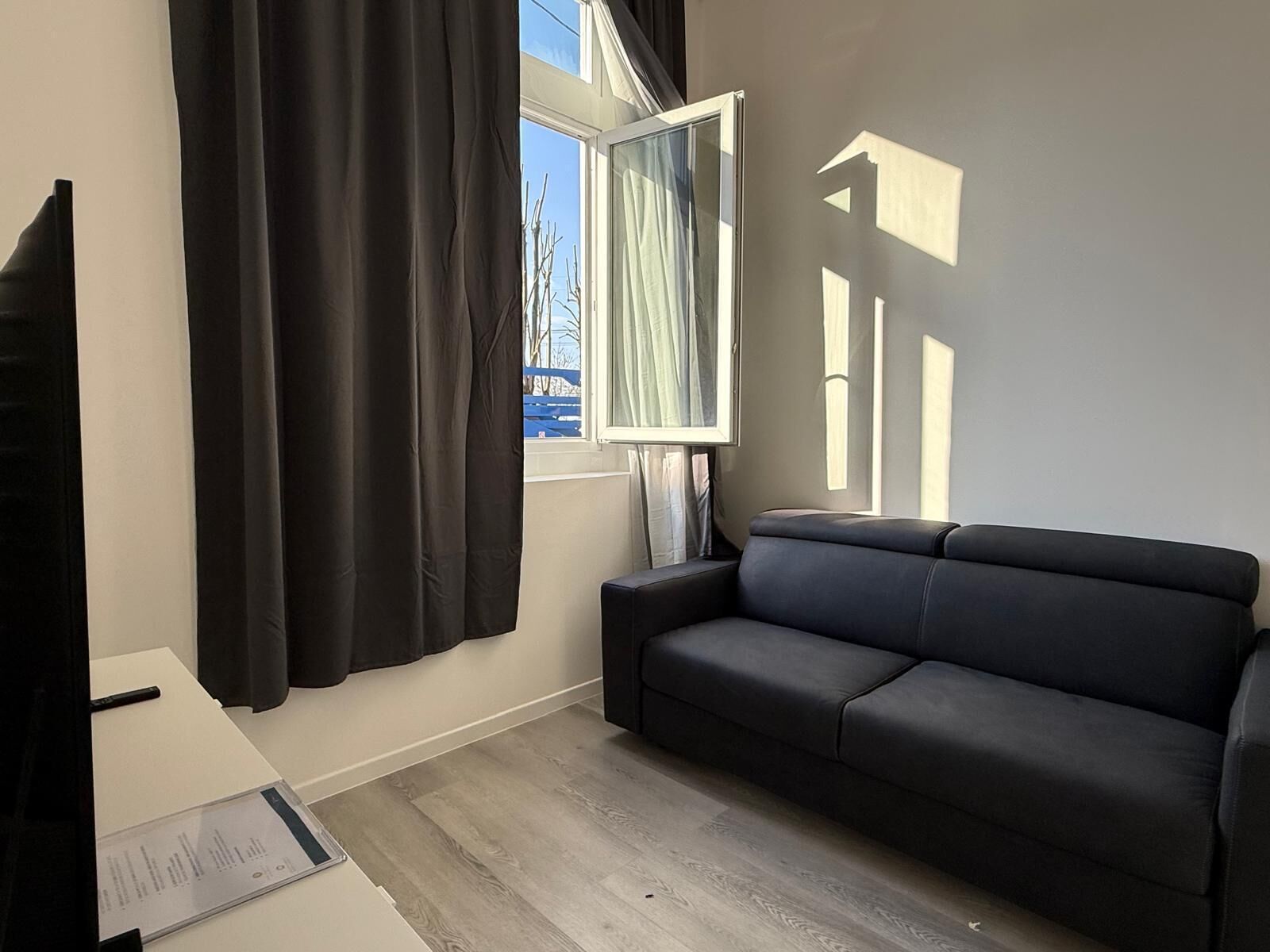 A modern living room with a dark sofa, a flat-screen TV, and a window with curtains.