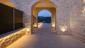 An arched stone corridor with a view of the landscape, illuminated by wall-mounted lights. - Luxury carob stone villa near Almyrida beach with private pool! (Gavalohori)