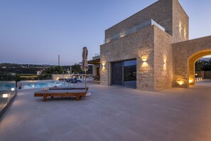 A modern building with a pool, lounge chairs, and outdoor seating. - Luxury carob stone villa near Almyrida beach with private pool! (Gavalohori)