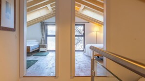 Ein modernes Interieur mit einer Treppe zu einem Dachzimmer mit Dachfenster, einem sichtbaren Bett und Blick ins Freie.