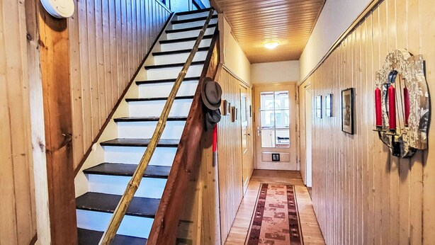 A wooden interior hallway with a staircase, a door with a window, and a wall-mounted fire extinguisher.