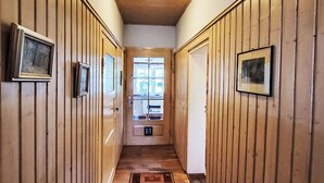 A hallway with wooden paneling, framed pictures on the walls, a wooden floor, and a ceiling light.