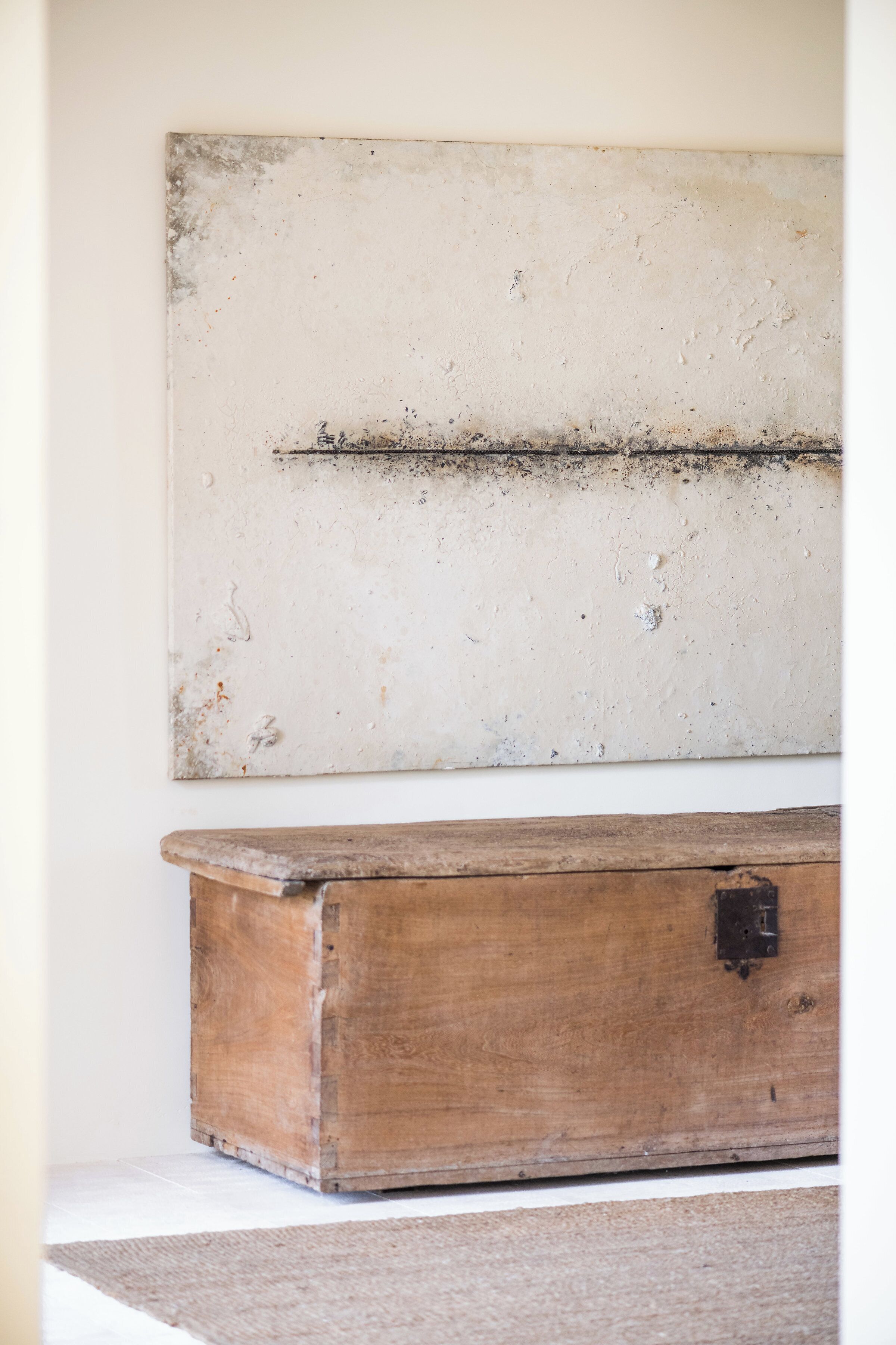 Un cofre de madera rústico frente a una pared lisa con una pizarra texturizada encima.