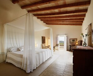 Quarto com cama de dossel, escrivaninha, cadeira e vista para o exterior.