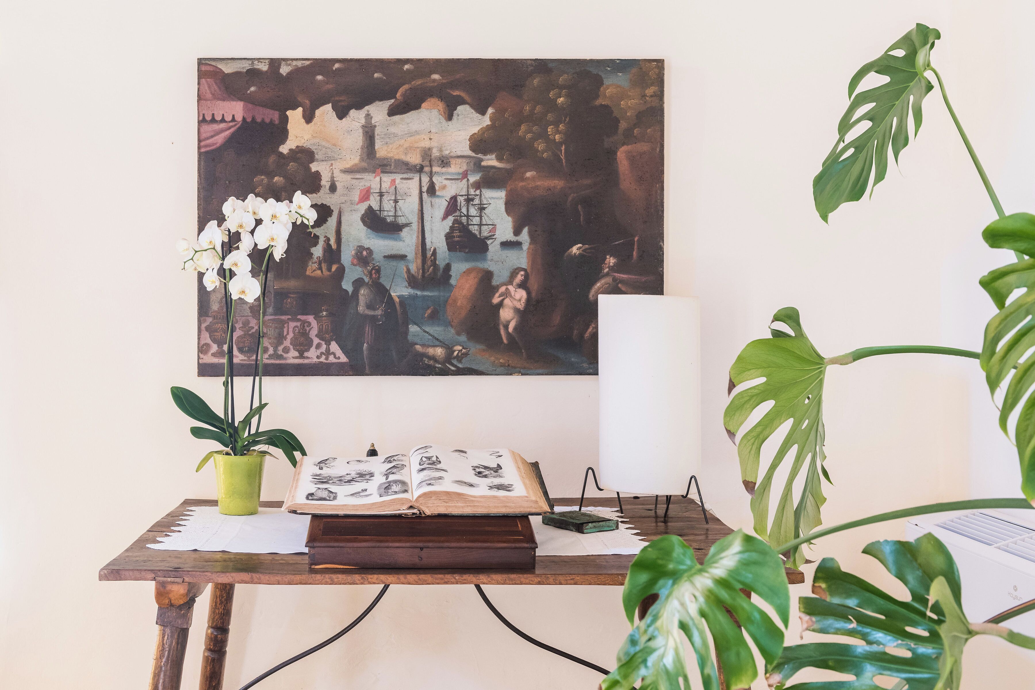 A wooden table with a book, a potted plant, and a painting.