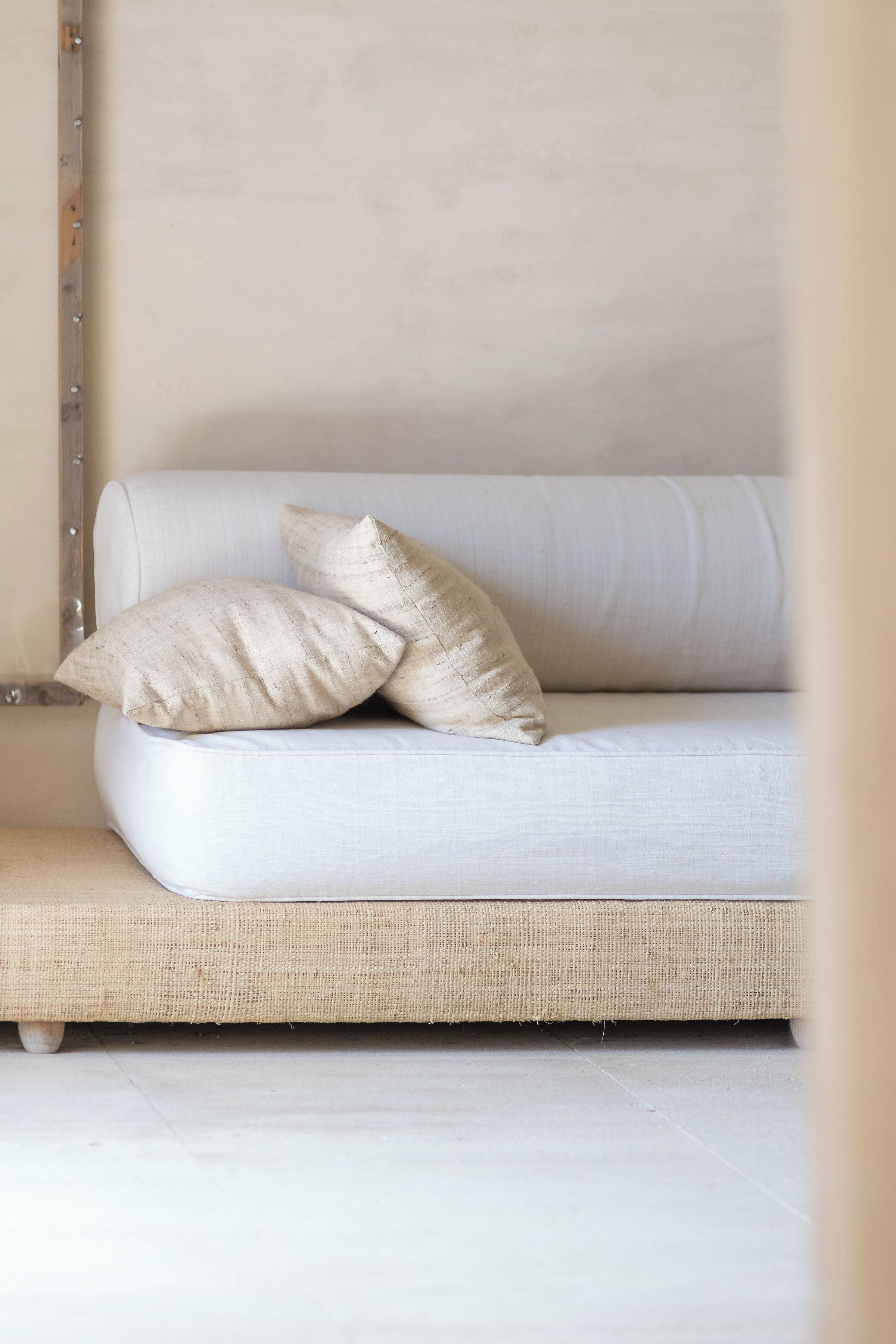 Un sofá blanco con dos almohadas color beige frente a una pared lisa.