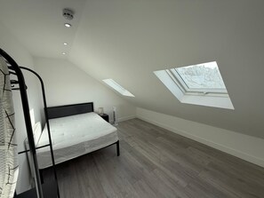 Une chambre avec un plafond en pente, un puits de lumière, un lit, un radiateur et une fenêtre.