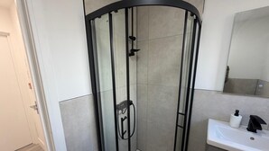 Ein modernes Badezimmer mit einer Duschkabine aus Glas, einem weißen Waschbecken und einem Spiegel darüber.