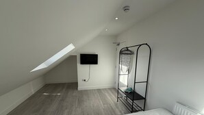 Ein Schlafzimmer mit schrägen Wänden, einem Bett, einem an der Wand befestigten Fernseher und einem Wäscheständer.