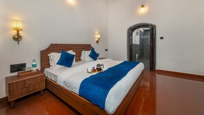 A neatly made bed with a blue blanket, a wooden nightstand with a water bottle, and two wall-mounted lamps. - Sherbaug Nature Park & Resort (Panchgani)