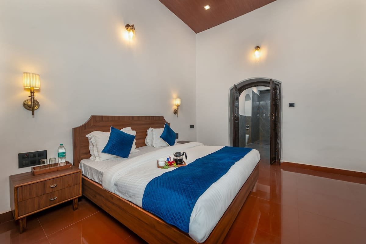 A neatly made bed with a blue blanket, a wooden nightstand with a water bottle, and two wall-mounted lamps.