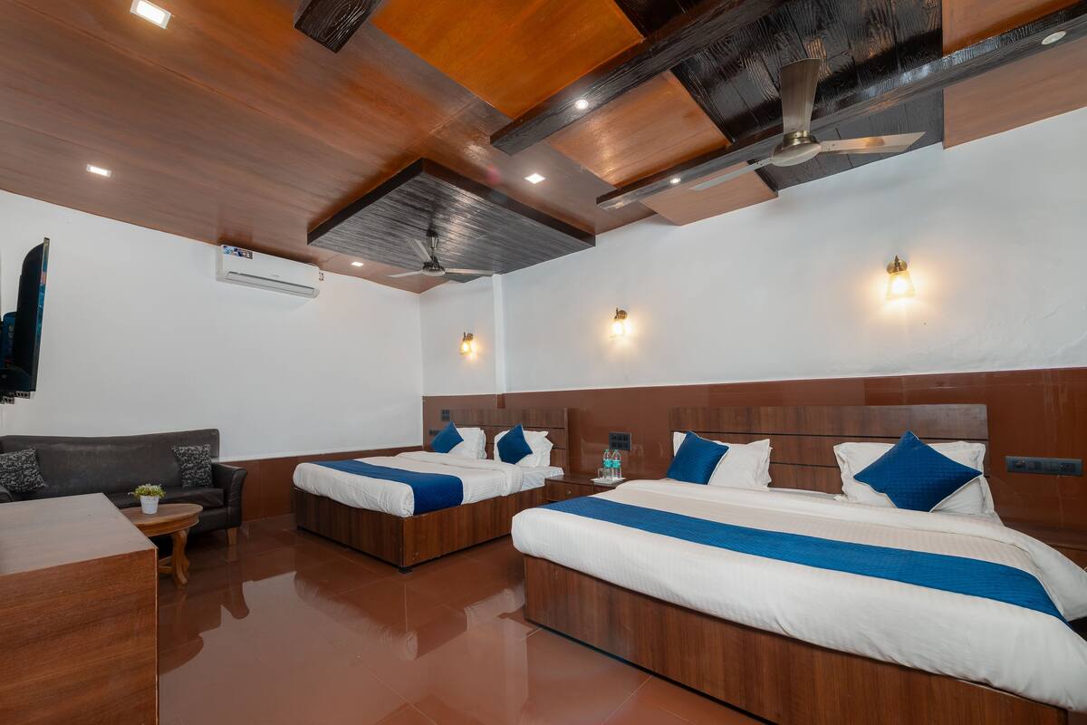 A hotel room with two beds, a sofa, a wooden coffee table, and a ceiling fan.