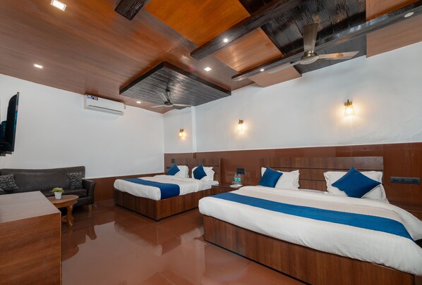 Habitación de hotel con dos camas, un sofá, una mesa de centro de madera y un ventilador de techo.